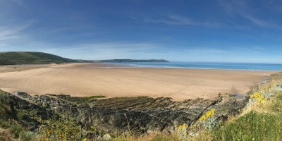 Photo of a clear beach with blue skies and green grass in the foreground overlooking the beach